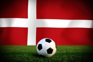 Fodbold på græsplæne med dansk flag i baggrunden